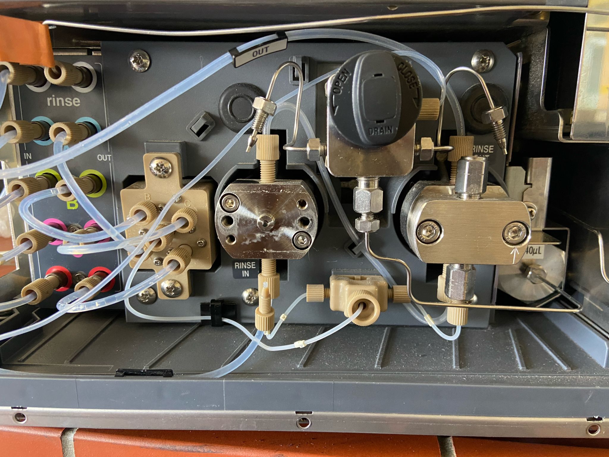 The pump head area of a Shimadzu i-Series HPLC with the cover off, showing the rinse ports, the drain valve and two check valve blocks. White crystalline deposit has built up on the face and around the screws of the left pump head.